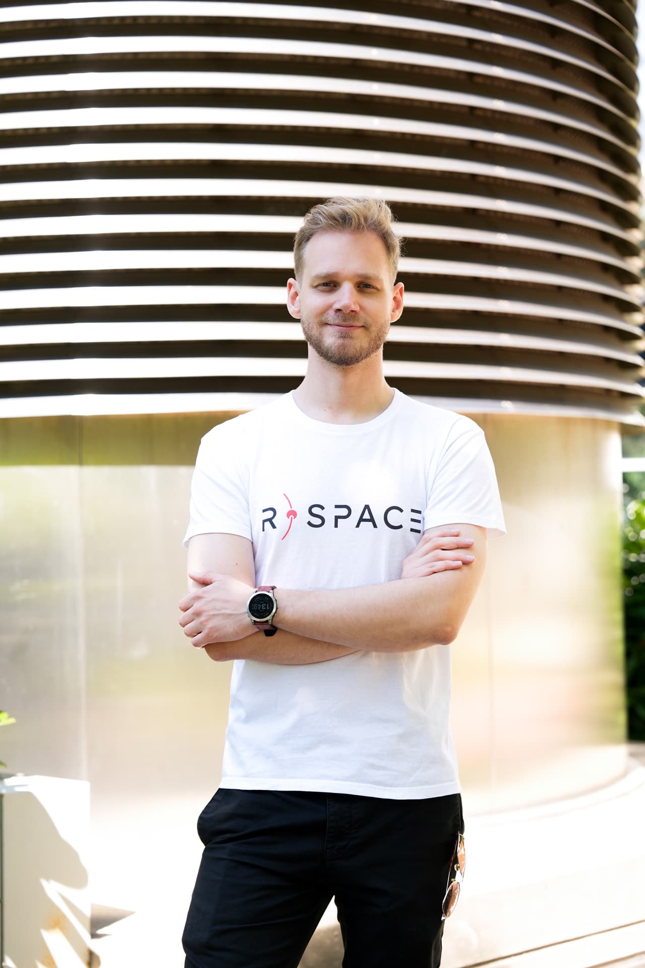 Person wearing an R-Space T-shirt standing next to a whiteboard with handwritten notes in a modern office setting.