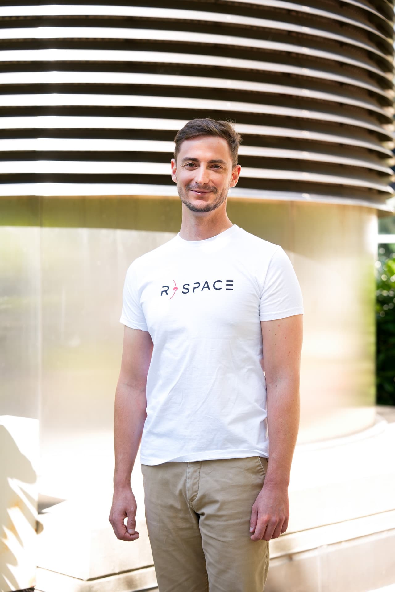 Person wearing an R-Space T-shirt standing next to a whiteboard with handwritten notes in a modern office setting.