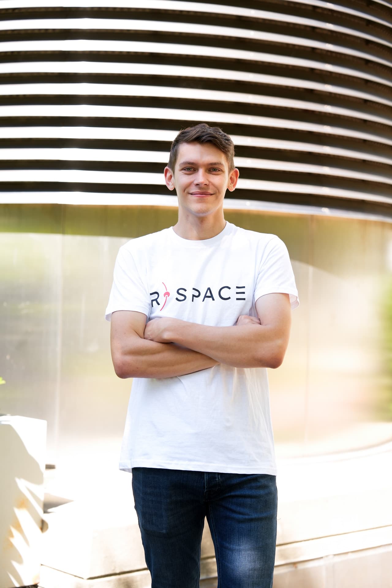 Person wearing an R-Space T-shirt standing next to a whiteboard with handwritten notes in a modern office setting.