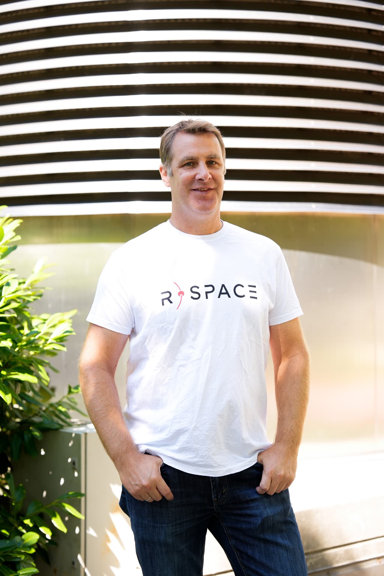 Person wearing an R-Space T-shirt standing next to a whiteboard with handwritten notes in a modern office setting.