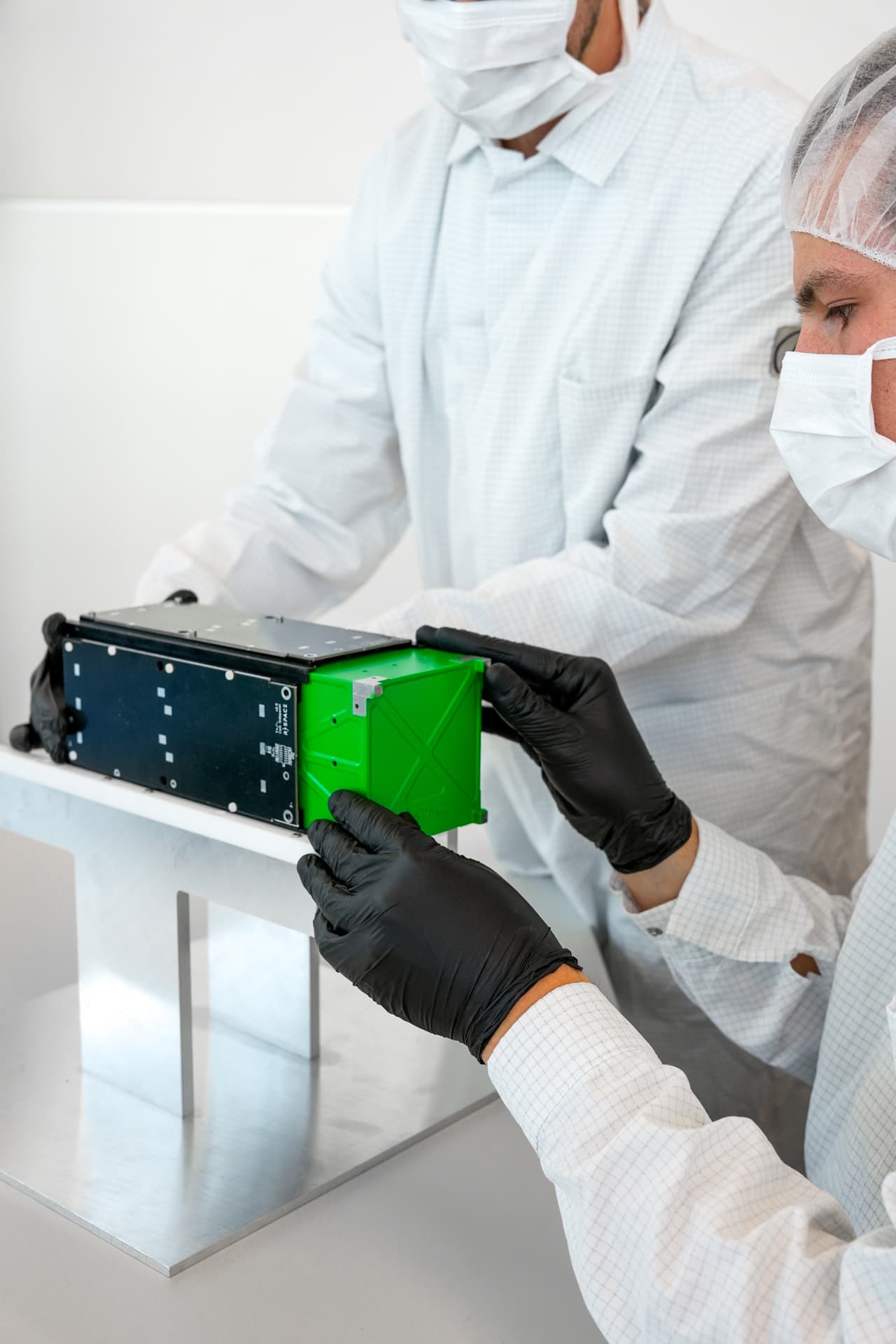 Engineer wearing gloves and safety glasses inspecting small electronic components through a magnifying lamp in a laboratory.