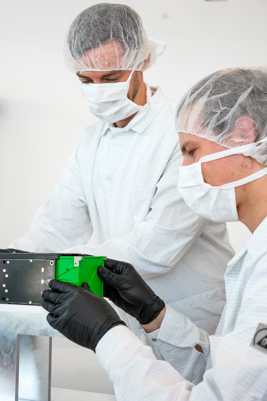 Engineer wearing gloves and safety glasses inspecting small electronic components through a magnifying lamp in a laboratory.