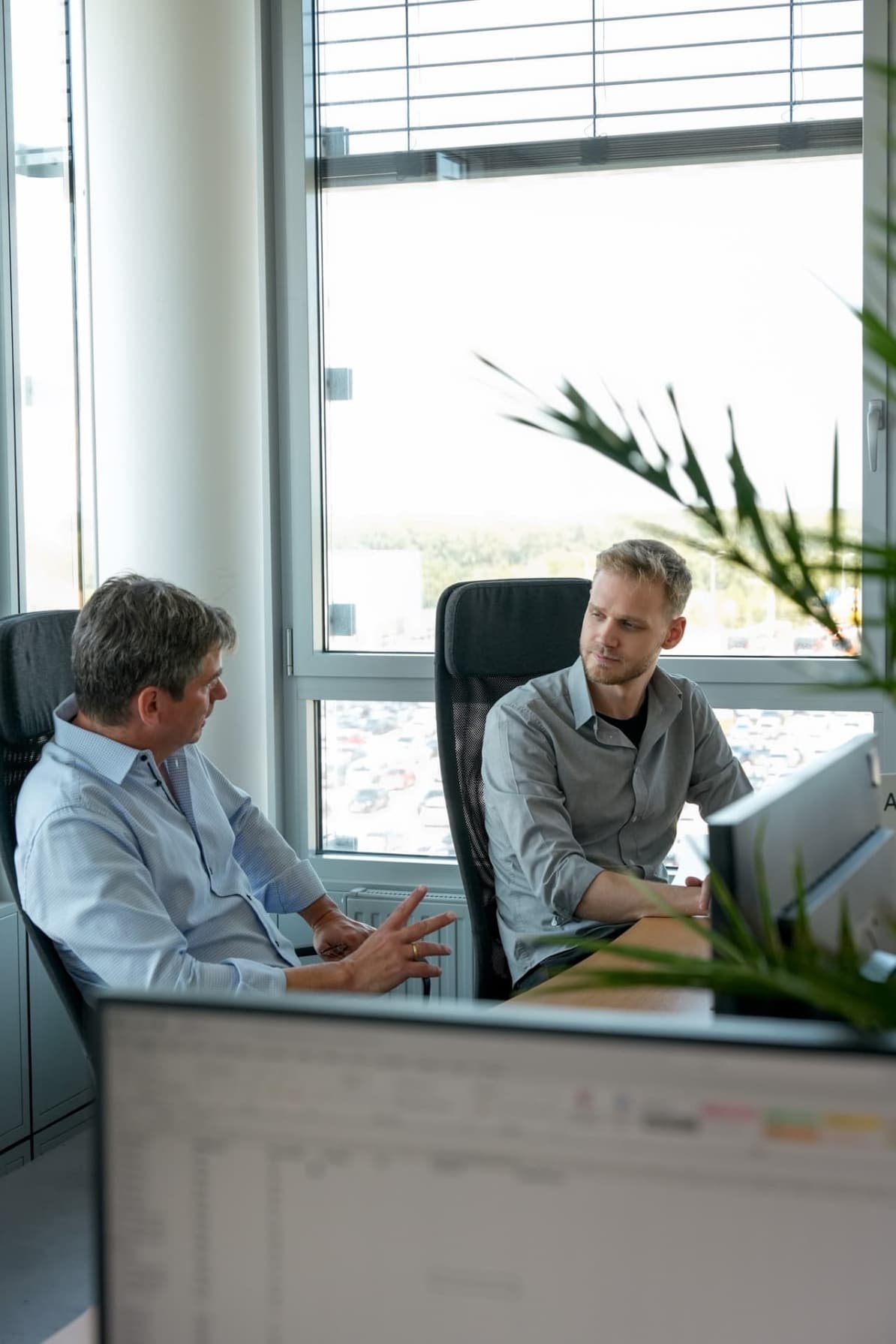 Two professionals having a focused discussion at a desk in a modern office with large windows and natural light.