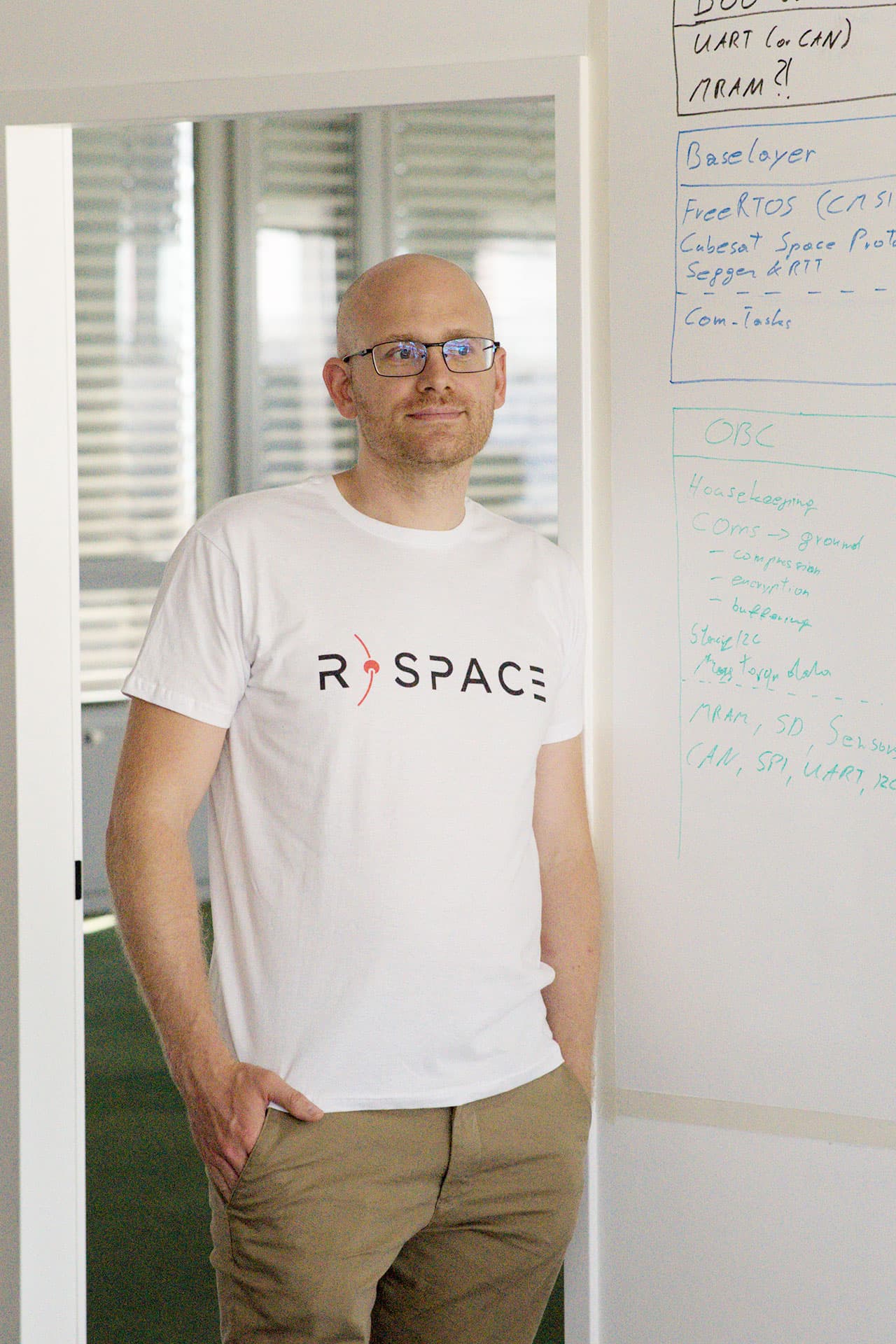 Person wearing an R-Space T-shirt standing next to a whiteboard with handwritten notes in a modern office setting.