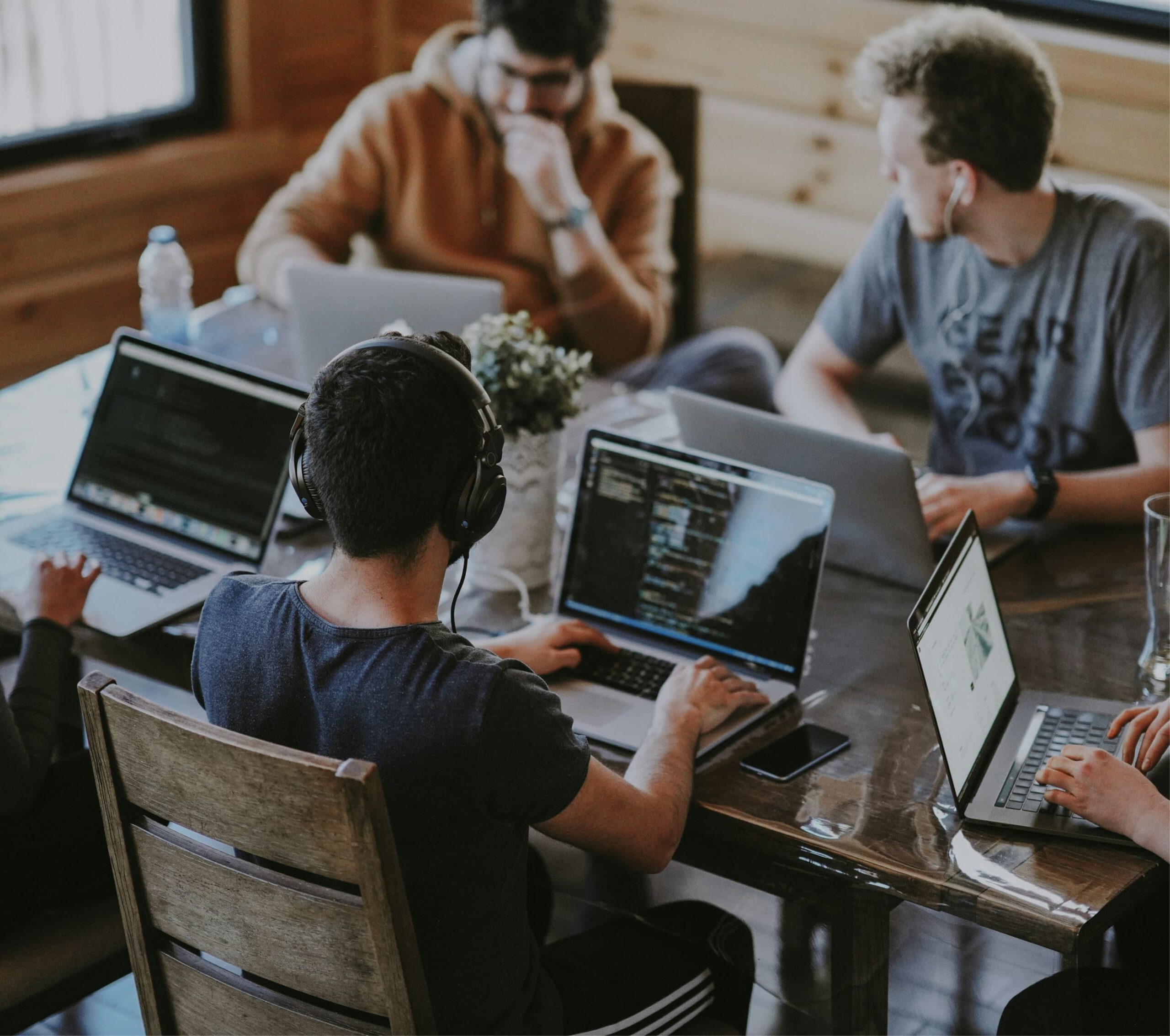 Group of young professionals working on laptops around a wooden table in a collaborative workspace.