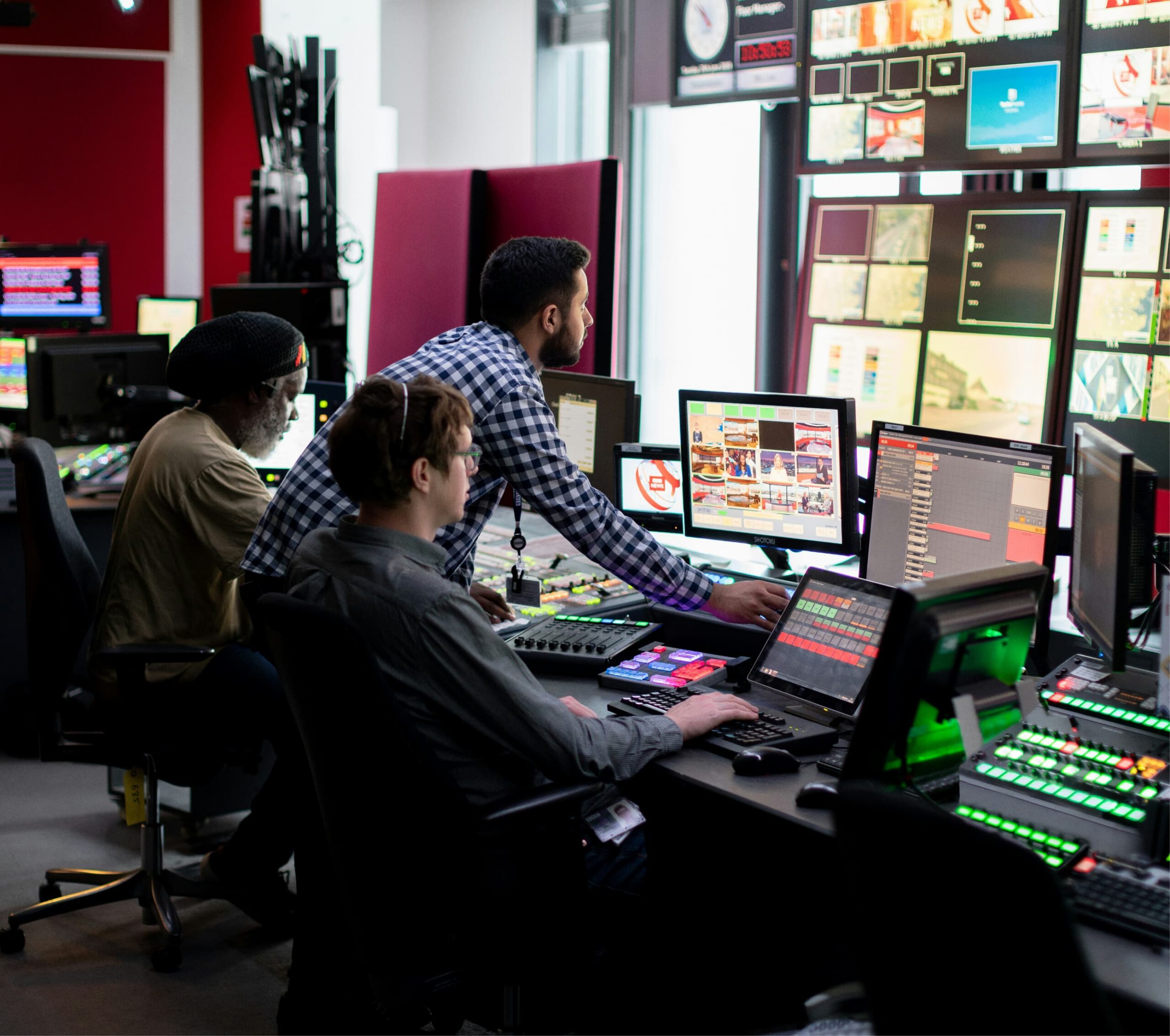 Team of technicians operating multiple screens and control panels in a high-tech broadcast or mission control room.